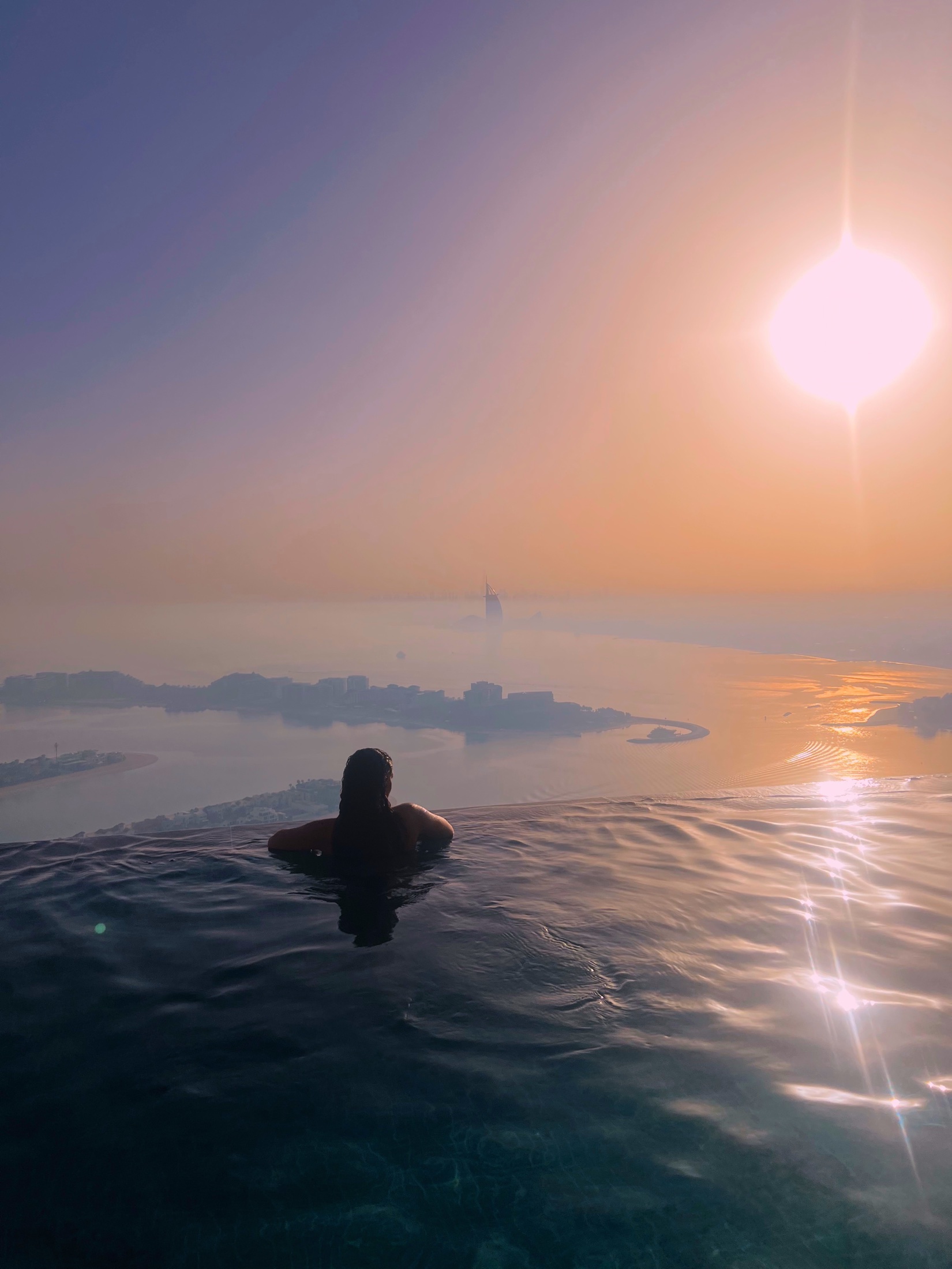 Silhouette in an infinity pool overlooking Dubai at sunset